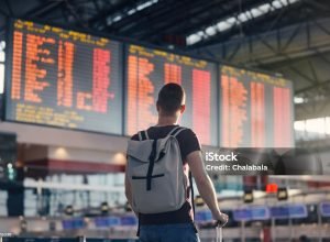 Traveling by airplane. Man walking with backpack and suitcase walking through airport terminal and looking at departure information.